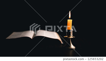 Dark, an antique candle cast its light on the old Bible, its flames flickering gently over the book on the table, symbolizing the enduring essence of religion. candle, bible, dark, light, book, old. 125653202