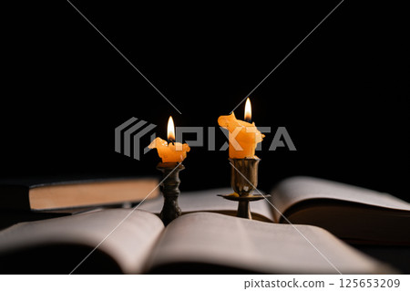 Dark, an antique candle cast its light on the old Bible, its flames flickering gently over the book on the table, symbolizing the enduring essence of religion. candle, bible, dark, light, book, old. 125653209
