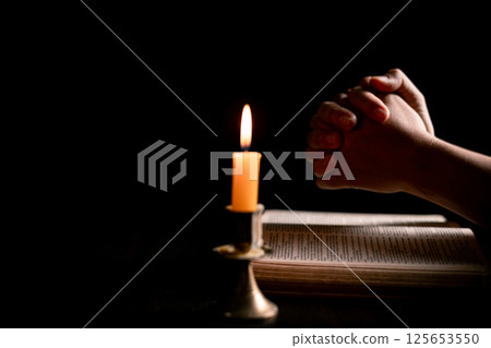 In the dark, hand clasped in prayer, illuminated by the soft candlelight, as black flames of candle fire flickered gently. candle, pray, hand, prayer, black, fire, flames, candlelight, light, dark. In the dark, hand clasped in prayer, illuminated by the soft candlelight, as black flames of candle fire flickered gently. candle, pray, hand, prayer, black, fire, flames, candlelight, light, dark. 125653550