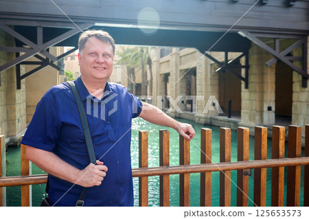 Adult blond man traveling in Venice, standing above water canal Adult blond man traveling in Venice, standing above water canal 125653573