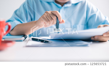 Notary placed their stamp of approval on the document as the lawyer and business person finalized the contract, ensuring all legal paperwork was in order. stamp, approval, document, contract, person. Notary placed their stamp of approval on the document as the lawyer and business person finalized the contract, ensuring all legal paperwork was in order. stamp, approval, document, contract, person. 125653721