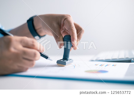 Notary placed their stamp of approval on the document as the lawyer and business person finalized the contract, ensuring all legal paperwork was in order. stamp, approval, document, contract, person. Notary placed their stamp of approval on the document as the lawyer and business person finalized the contract, ensuring all legal paperwork was in order. stamp, approval, document, contract, person. 125653772