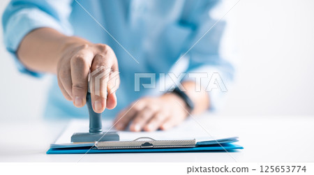 Notary placed their stamp of approval on the document as the lawyer and business person finalized the contract, ensuring all legal paperwork was in order. stamp, approval, document, contract, person. 125653774