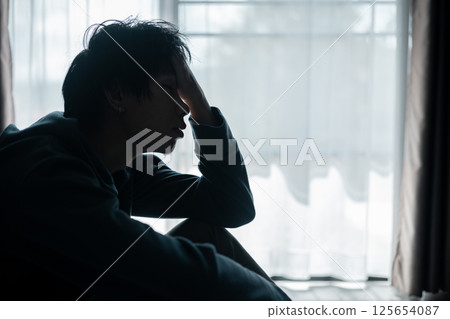 Silhouette of lost cast long shadow, embodying deep despair and hopelessness left him feeling perpetually stressed, sad, and unhappy. man sat alone, feeling weight of anxiety, stress, and depression. 125654087