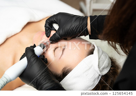 A close-up cosmetologist manipulates a hydropeeling machine to clean and rejuvenate a patient's skin in a modern clinic. A close-up cosmetologist manipulates a hydropeeling machine to clean and rejuvenate a patient's skin in a modern clinic. 125654145