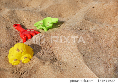 Bright plastic toys, including a car mold and rake, lie scattered on warm beach sand. Bright plastic toys, including a car mold and rake, lie scattered on warm beach sand. 125654682