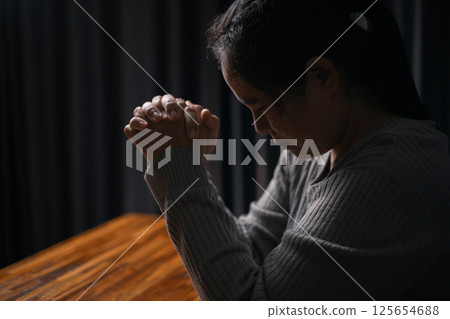 Woman bowed her head in prayer, her hand clasped in faith, as she prayed to Jesus Christ for hope, peace, and the guiding presence of God in her religion. god, religion, faith, hope, peace, christian. 125654688