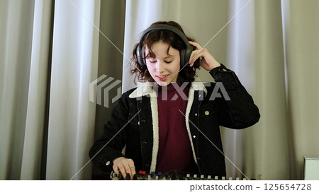 A girl adjusts a sound mixer while singing, her headphones emphasizing the focus on audio. The photo captures the joy of engaging in creative and musical tasks. 125654728