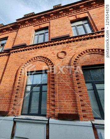 Low-angle view of a red brick building with ornate arches and black-framed windows. The image showcases architectural heritage and craftsmanship of traditional masonry. 125654878
