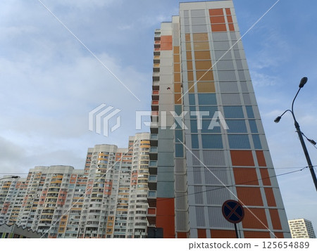 A large multi-story residential building with a pastel color palette of pink, white, and blue, featuring numerous balconies. The high-rise structure represents modern city living with an expansive 125654889