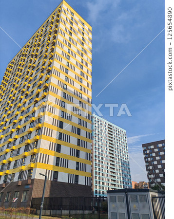 Two modern high-rise apartment buildings, one with a yellow and white facade, and the other with a dark and light checkerboard design. The contrasting geometric patterns reflect contemporary urban 125654890
