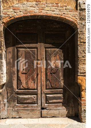 weathered wooden door in rustic stone archway 125654979