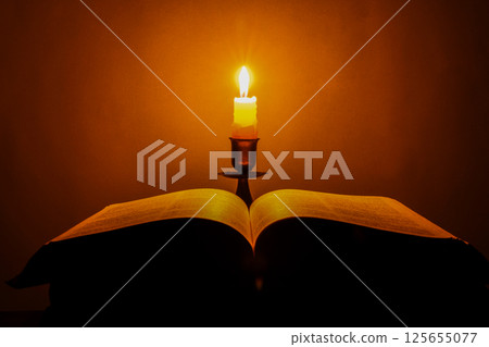 Candle with bible on a old oak wooden table. Beautiful gold background. Religion concept. 125655077