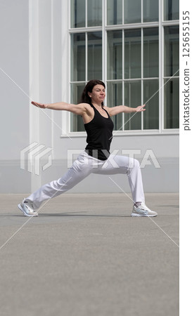 A fit woman stretches into a powerful yoga stance, maintaining focus and control. This scene represents discipline, body awareness, and the art of self-improvement. 125655155