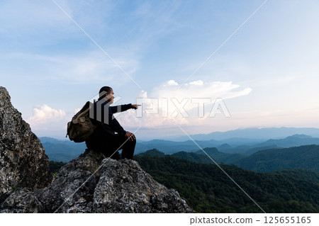 Male tourist on top of rocky mountain. A peaceful man meditating yoga relaxing alone sitting on a mountain top at sunrise with nature landscape. Male tourist on top of rocky mountain. A peaceful man meditating yoga relaxing alone sitting on a mountain top at sunrise with nature landscape. 125655165
