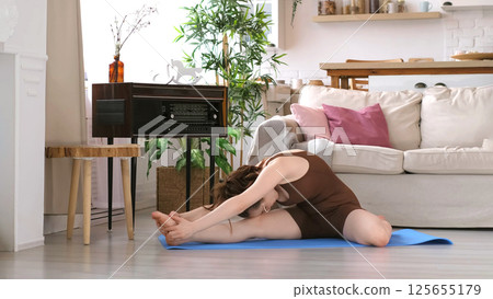 A serene woman practices yoga in her stylish living room, emphasizing balance and mindfulness. This photograph speaks to the trend of integrating wellness routines into daily home life. 125655179