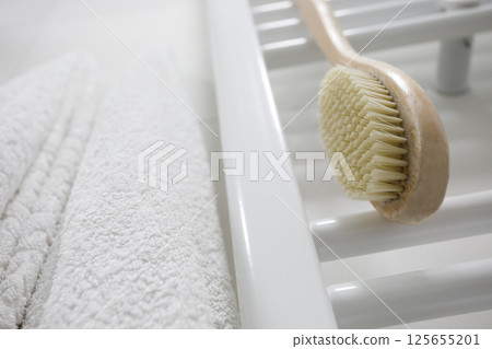Heated towel rail, wooden brush and white cotton towel close-up 125655201