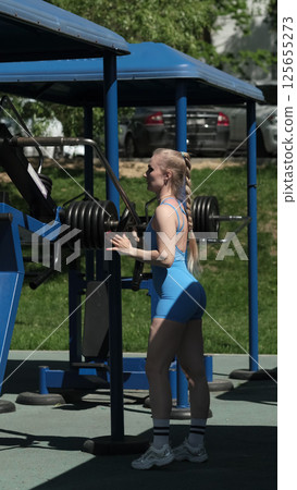 A woman in a blue sports outfit is seen adjusting weights on a machine at an outdoor gym, showcasing her commitment to strength training. This image highlights the importance of outdoor fitness A woman in a blue sports outfit is seen adjusting weights on a machine at an outdoor gym, showcasing her commitment to strength training. This image highlights the importance of outdoor fitness 125655273