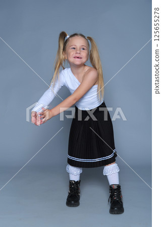 little girl poses energetically in the studio, raising her fists with a playful smile. Her outfit and pose convey both style and fun, making this image perfect for children's fashion and lifestyle 125655278