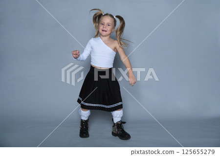 little girl poses energetically in the studio, raising her fists with a playful smile. Her outfit and pose convey both style and fun, making this image perfect for children's fashion and lifestyle 125655279