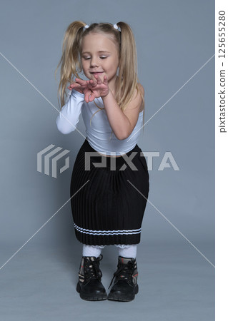 A little girl expresses her playful side with a fun, energetic pose in a studio setting. The image captures the vibrant energy of childhood, paired with a stylish and modern look. 125655280