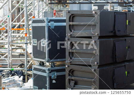 Stacks of sound equipment and lighting gear are arranged at an outdoor venue, ready for a concert. Stacks of sound equipment and lighting gear are arranged at an outdoor venue, ready for a concert. 125655750