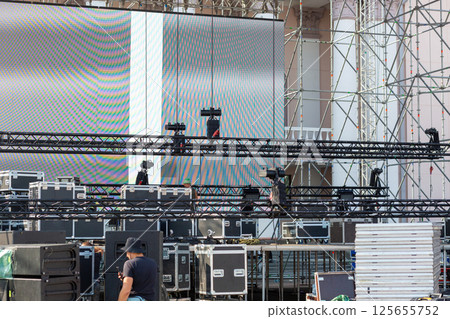 Stacks of sound equipment and lighting gear are arranged at an outdoor venue, ready for a concert. Stacks of sound equipment and lighting gear are arranged at an outdoor venue, ready for a concert. 125655752