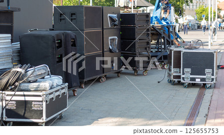 A collection of gear boxes and audio equipment arranged on carts, prepared for an outdoor concert setup A collection of gear boxes and audio equipment arranged on carts, prepared for an outdoor concert setup 125655753