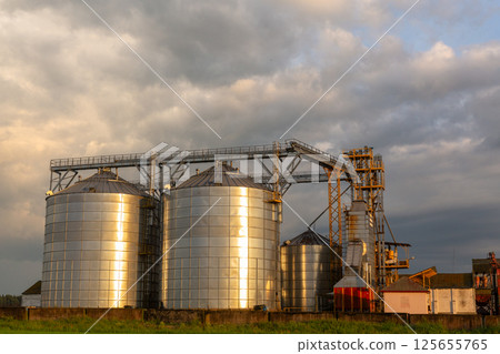 Group of grain dryers complex on dramatic cloudy sunset sky. 125655765