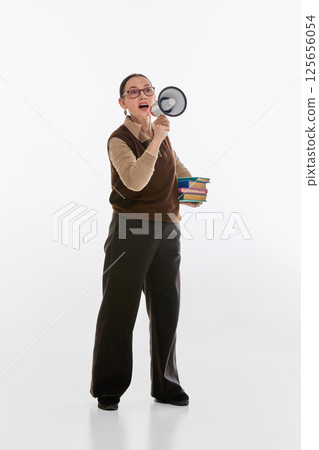 Older woman holding books and megaphone, appearing to make academic announcement against white studio background. Older woman holding books and megaphone, appearing to make academic announcement against white studio background. 125656054