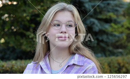 A young woman with glasses and a plaid shirt gazes thoughtfully into the distance in a serene outdoor setting. This photo captures calmness and the quiet beauty of contemplation. A young woman with glasses and a plaid shirt gazes thoughtfully into the distance in a serene outdoor setting. This photo captures calmness and the quiet beauty of contemplation. 125656297