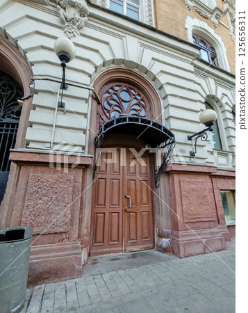 An aged wooden door surrounded by carved stonework and topped with a wrought-iron canopy. The image conveys themes of timeless design and urban heritage. 125656311