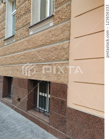 Close-up of a peach-colored building featuring intricate stone textures, decorative window moldings, and a mounted security camera. The photo highlights the contrast between old-world charm and modern 125656333