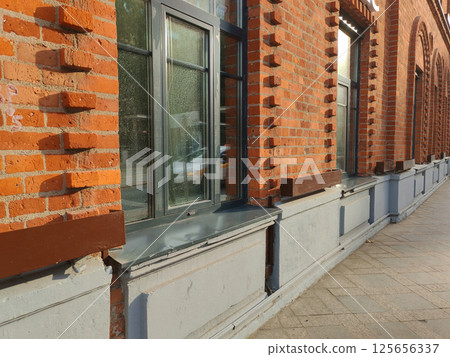 Close-up of a historic red brick building facade with arched windows and intricate masonry details. The perspective highlights the texture and craftsmanship of the exterior architecture. 125656337