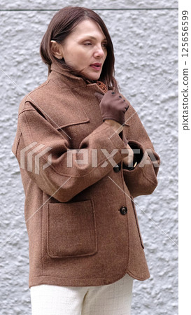 The natural beauty of a mature woman captured as she wraps herself in a coat. Emphasizes the importance of self-care during life transitions such as hormonal changes. 125656599