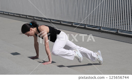 A fit woman engages in a high-intensity workout, executing mountain climbers with precision. The urban setting adds a sense of determination and discipline to the scene. 125656744