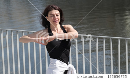 A fit woman practices a flowing movement by the water, her focused expression highlighting balance and control. The growing interest in holistic training emphasizes the harmony between body and mind. 125656755