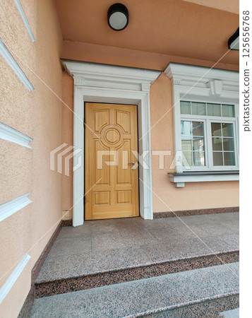 An ornate wooden door in a textured peach building featuring decorative stone and window details. The image reflects the balance of aesthetic charm and durability in urban architecture. An ornate wooden door in a textured peach building featuring decorative stone and window details. The image reflects the balance of aesthetic charm and durability in urban architecture. 125656768