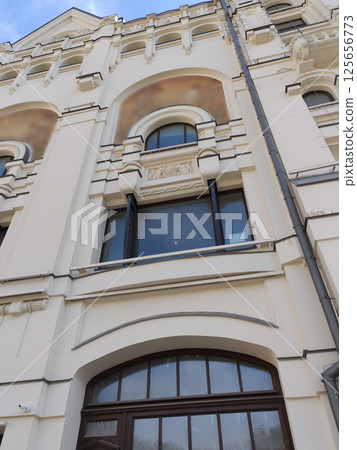 A close-up of a historic building facade featuring large arched windows, intricate decorative details, and a light beige finish. The design emphasizes classical architectural refinement. 125656773
