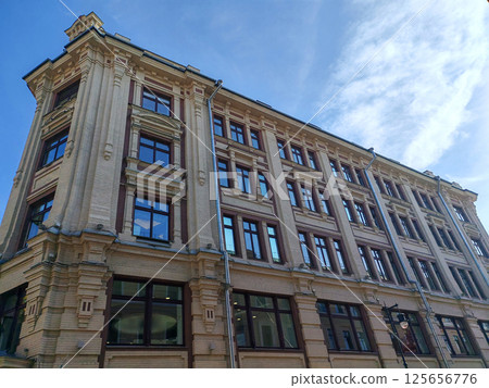 An elegant historic building with intricate brickwork and large windows reflecting the blue sky. The architectural grandeur suggests a story of urban development and hidden histories. An elegant historic building with intricate brickwork and large windows reflecting the blue sky. The architectural grandeur suggests a story of urban development and hidden histories. 125656776