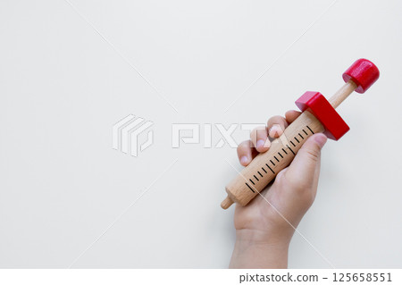 Child hand holding wooden toy syringe with red accents on white background 125658551