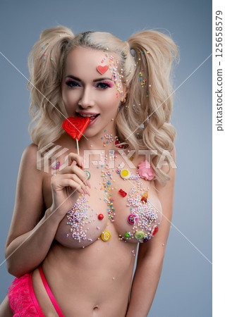 Woman with colorful body art and candy-themed accessories in playful pose 125658579