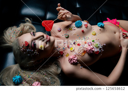 Captivating woman showcases body art with colorful sweets and tattoos 125658612