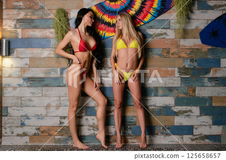 Two women posing confidently in vibrant lingerie by a textured wall 125658657