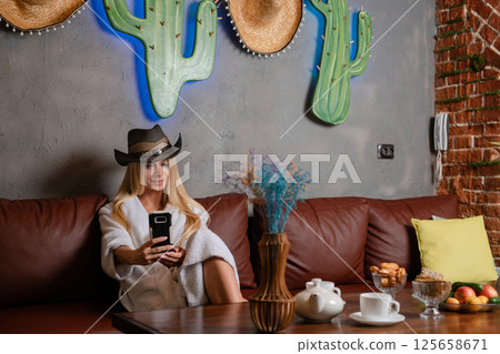 Elegant woman poses in lingerie with cowboy hat in stylish lounge setting 125658671