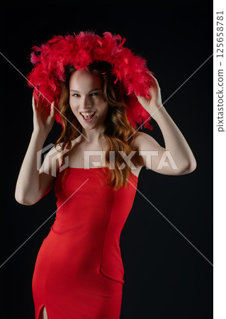 Woman posing confidently in a red dress with a vibrant feathered hat in a studio setting showcasing fun and emotion 125658781