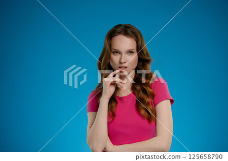 Woman with long hair expressing emotion while posing in a studio setting with a bright blue background 125658790