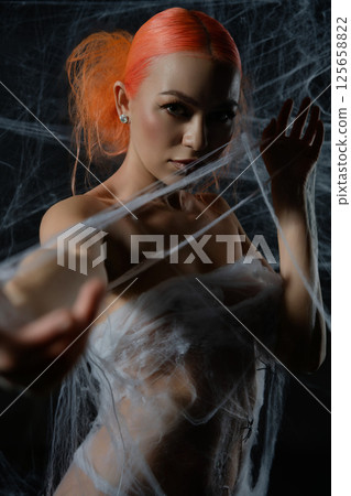 Red-haired woman ensnared in a delicate net trap amidst a dark background 125658822
