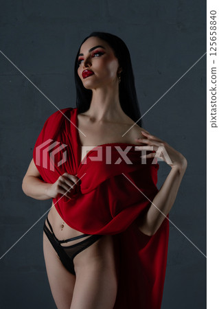 Elegant woman poses in red cloth and black lingerie against a dark background 125658840