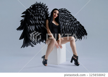 Woman in black lingerie with striking wings poses confidently indoors Woman in black lingerie with striking wings poses confidently indoors 125658842